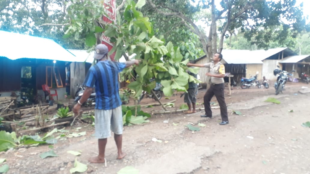 Brigpol Yohanes Namang membantu menebang pohon di pekarangan rumah warga